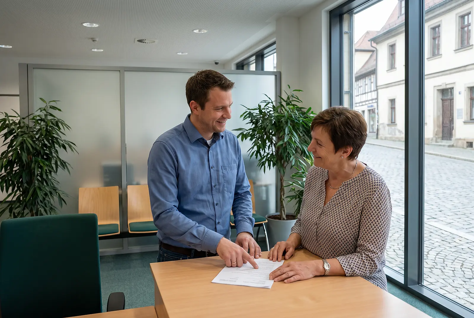 Sachbearbeiter bespricht mit einer Bürgerin Unterlagen im Bürgerbüro einer Stadtverwaltung
