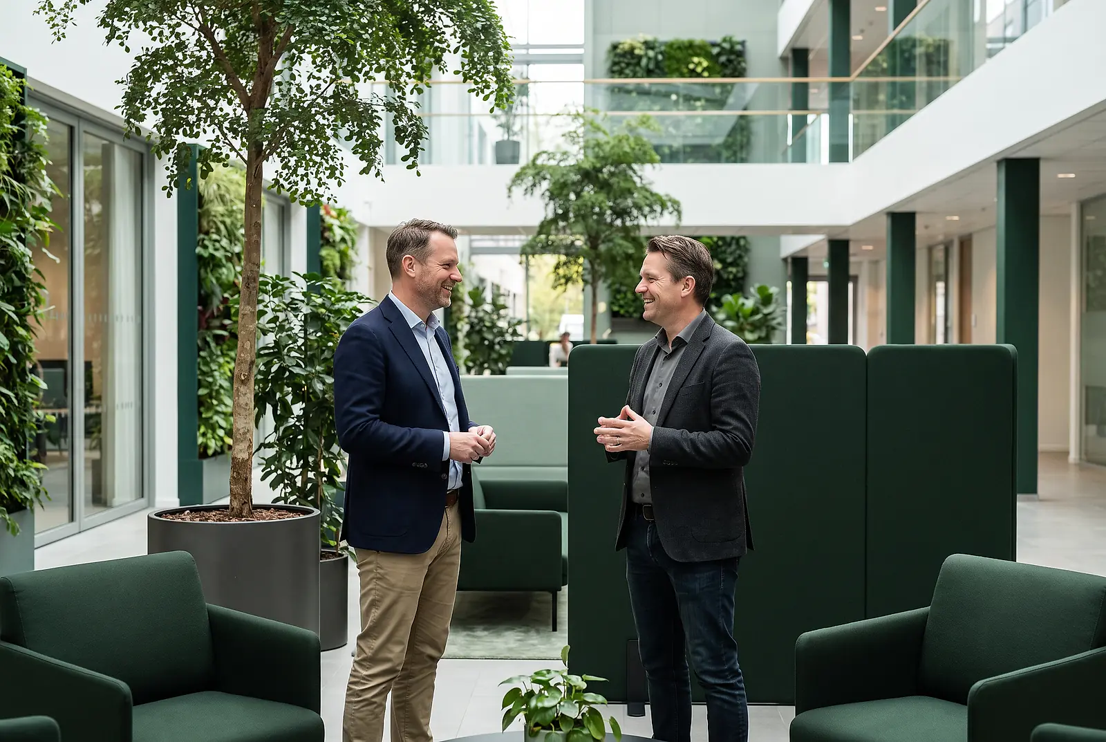 Zwei Führungskräfte stehen in einem begrünten Büroatrium und sprechen über nachhaltige ESG-Vorteile durch eine bKV