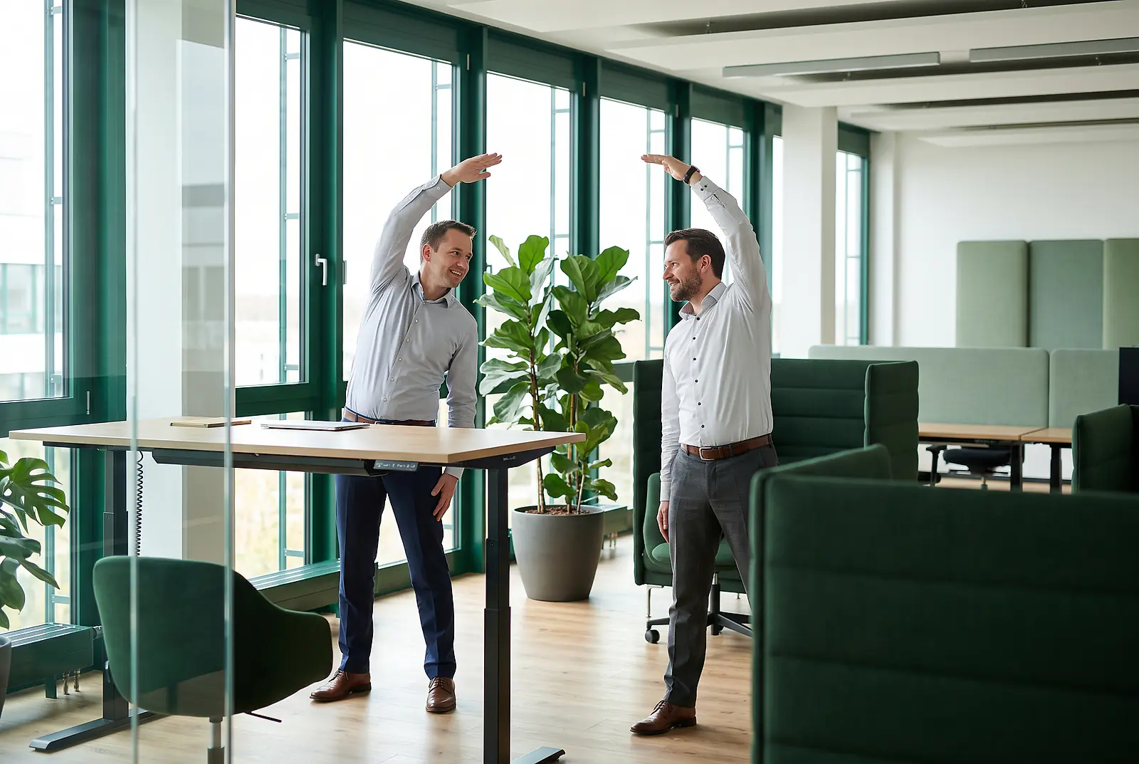 Zwei Mitarbeiter führen im Büro Dehnübungen für einen gesunden Rücken im Rahmen steuerfreier BGM-Leistungen aus