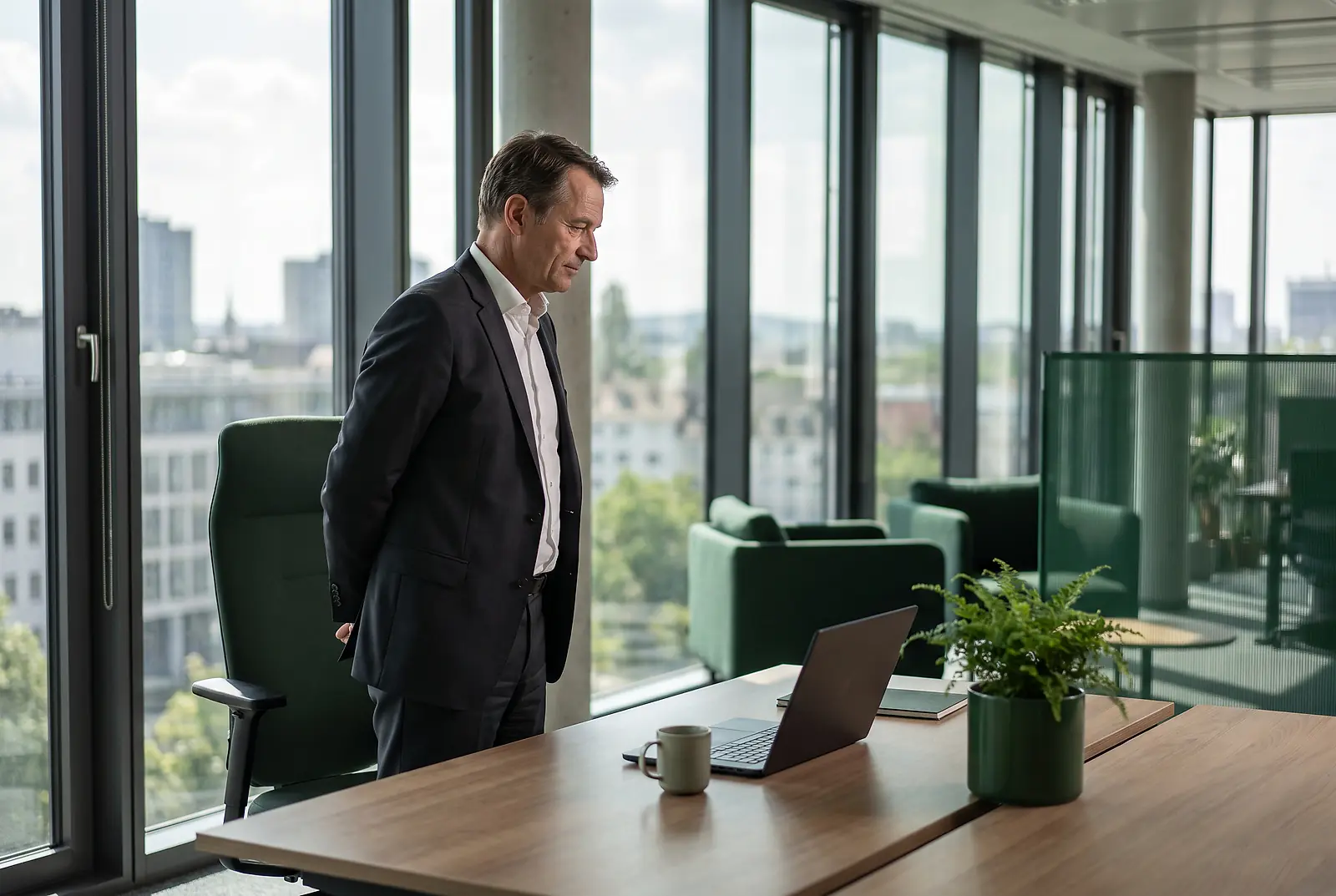 Ein Geschäftsmann im Anzug blickt im Büro nachdenklich auf einen verwaisten Arbeitsplatz mit leerem Bürostuhl