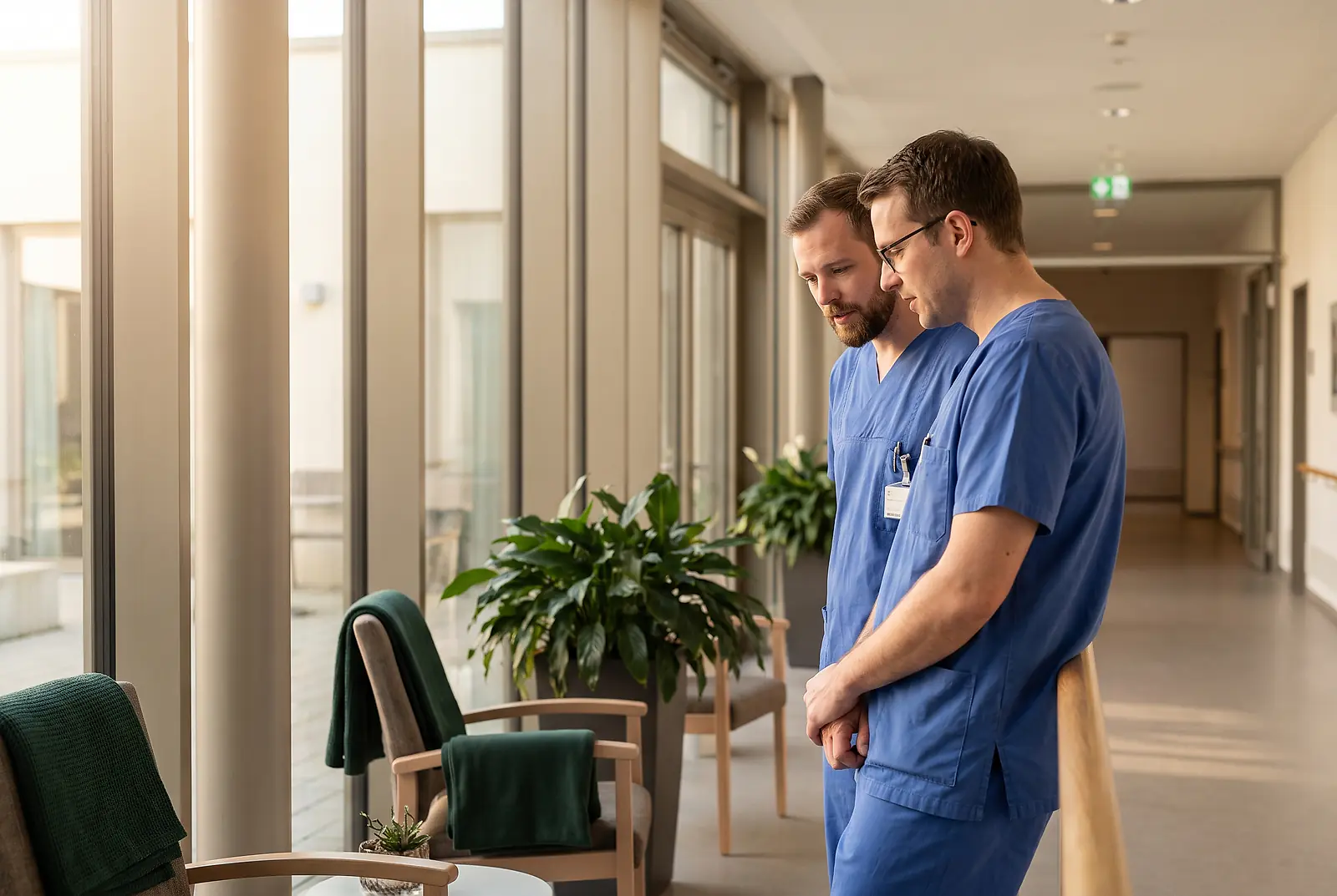 Zwei Pflegekräfte in blauer Arbeitskleidung unterhalten sich im Flur eines modernen Seniorenheims