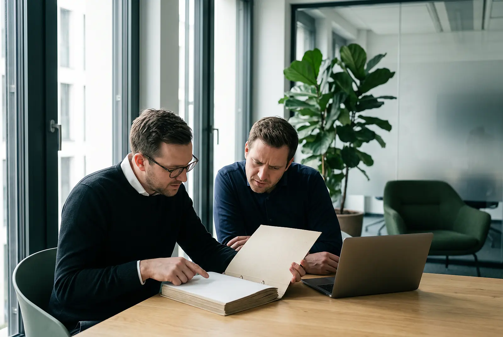 Zwei Kollegen sitzen am Bürotisch und gehen gemeinsam einen aufgeschlagenen Ordner durch