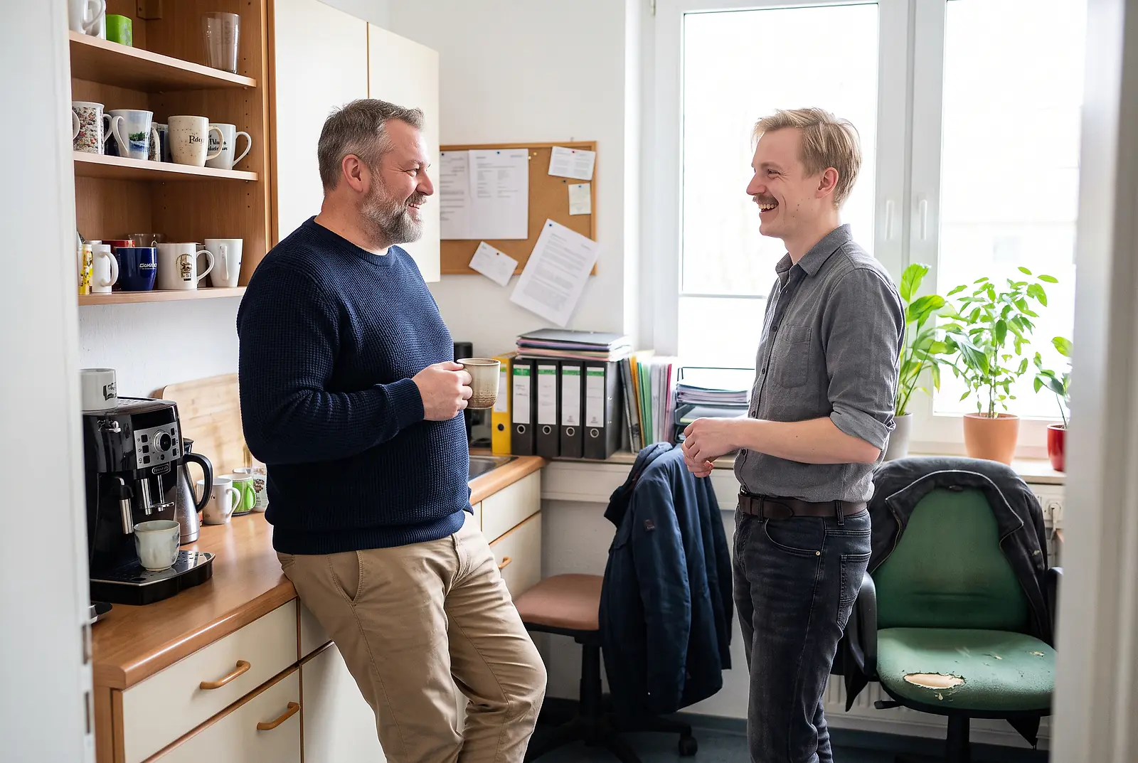 Zwei Kollegen in der Büroküche bei einer kurzen Kaffeepause im Gespräch